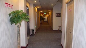 A hotel hallway with a potted plant, a trash bin, and a sign with a phone number.