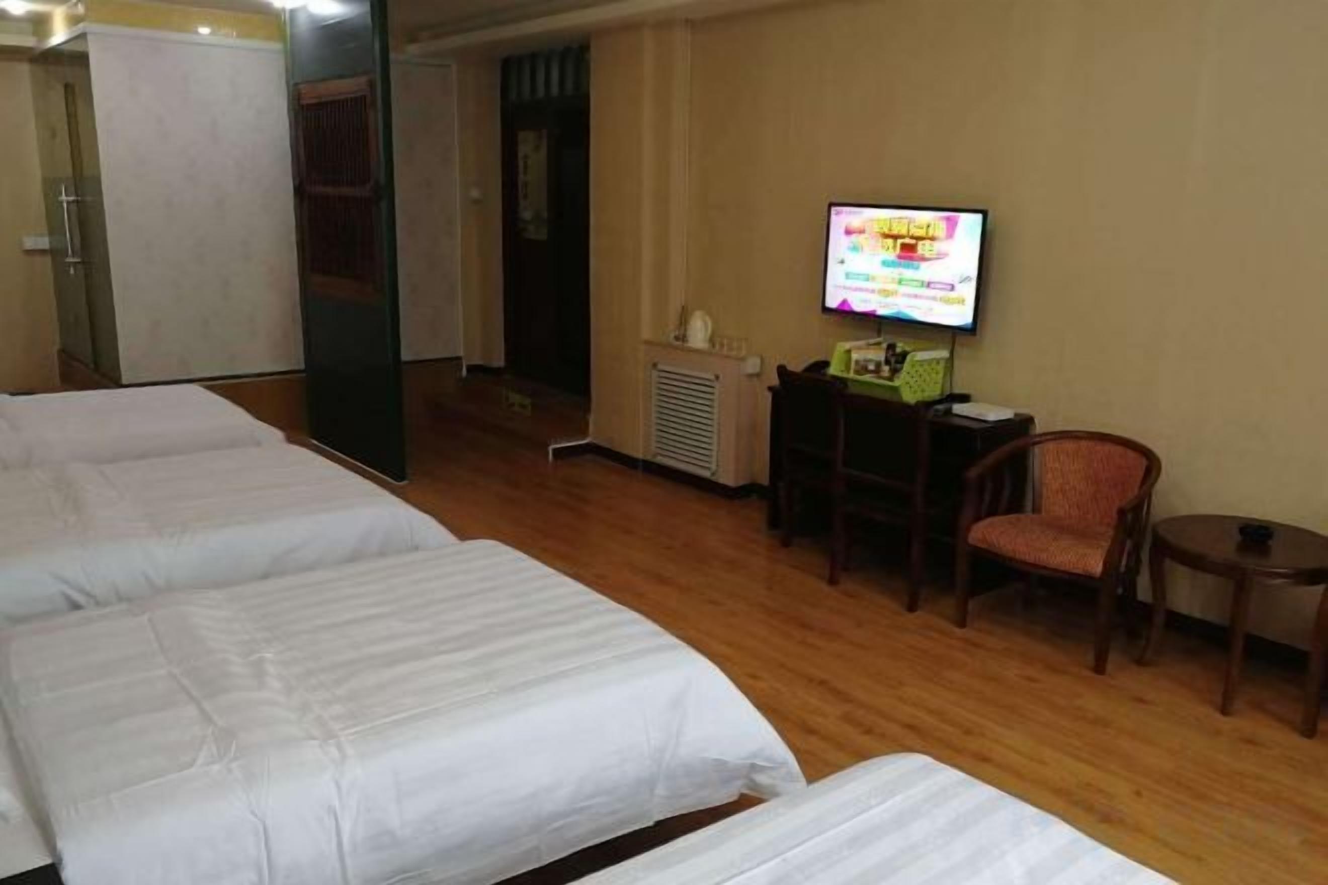 A hotel room with three beds, a television, a desk with a computer, and a chair.