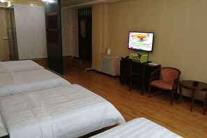 Een hotelkamer met drie bedden, een televisie, een bureau met een computer en een stoel.