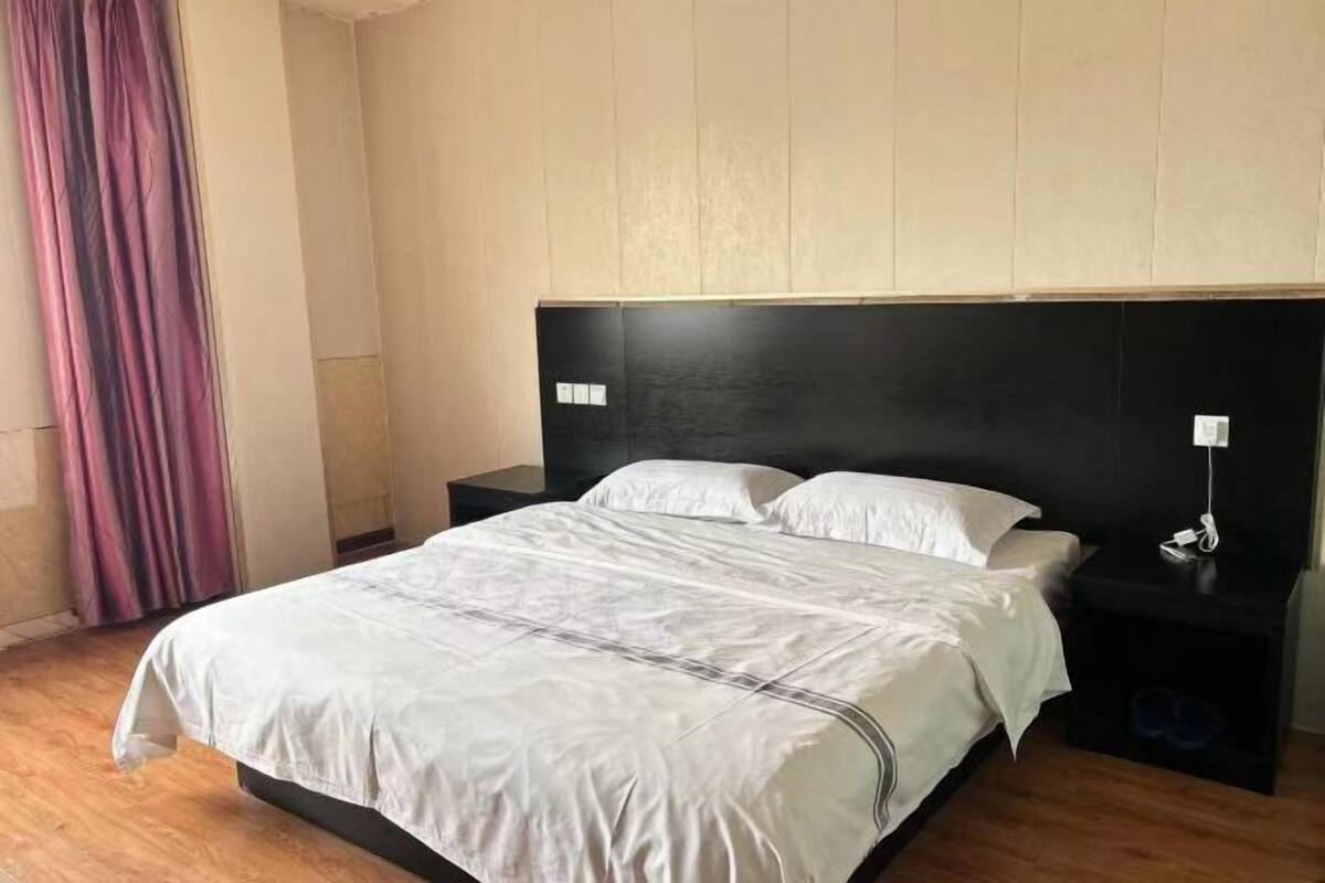 Habitación de hotel con cama, mesitas de noche, suelo de madera y una cortina.