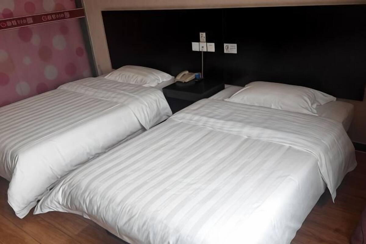 Habitación de hotel con dos camas, cabecera negra y suelo de madera.