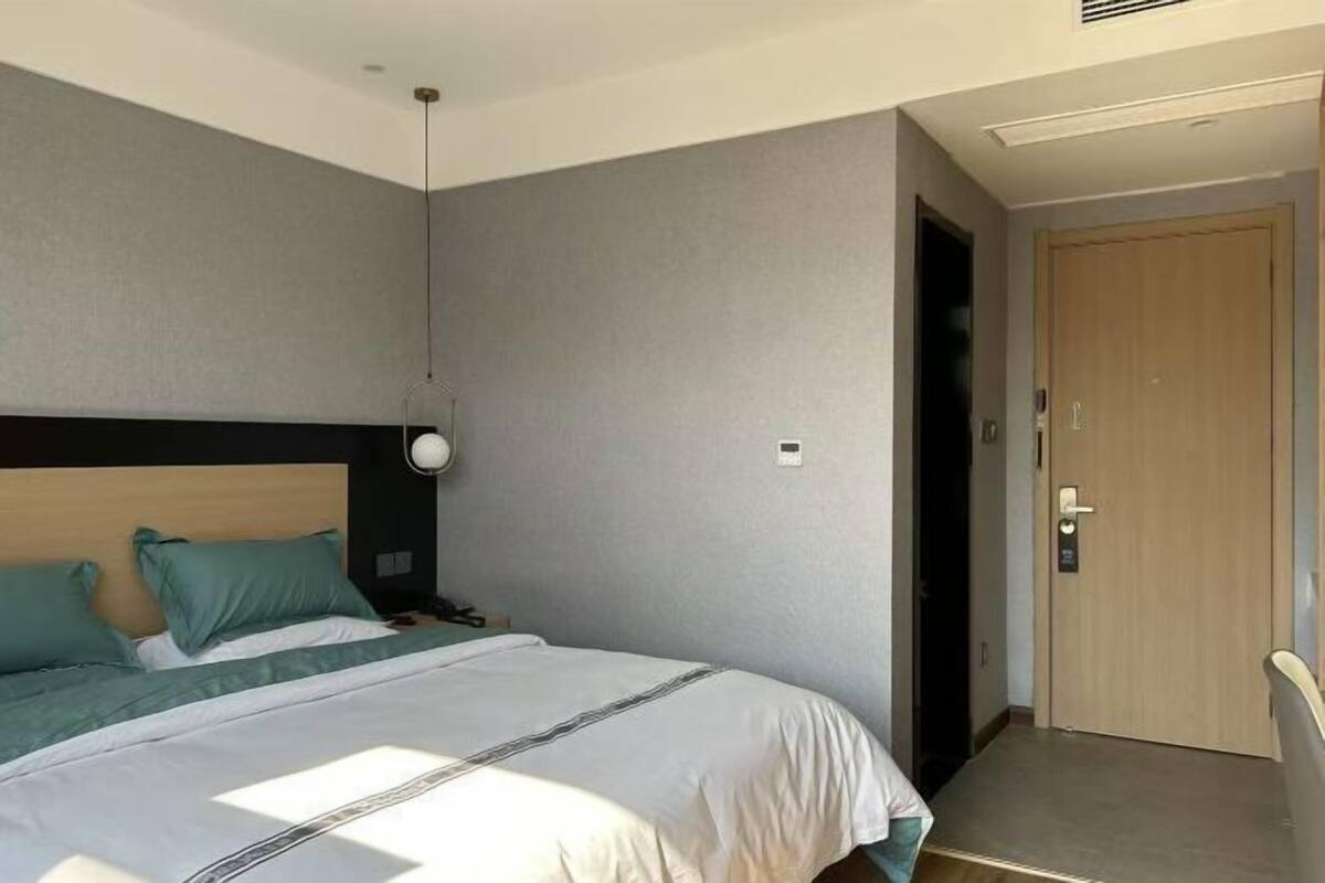 Habitación de hotel con cama, mesita de noche, lámpara, puerta y lámpara fijada a la pared.