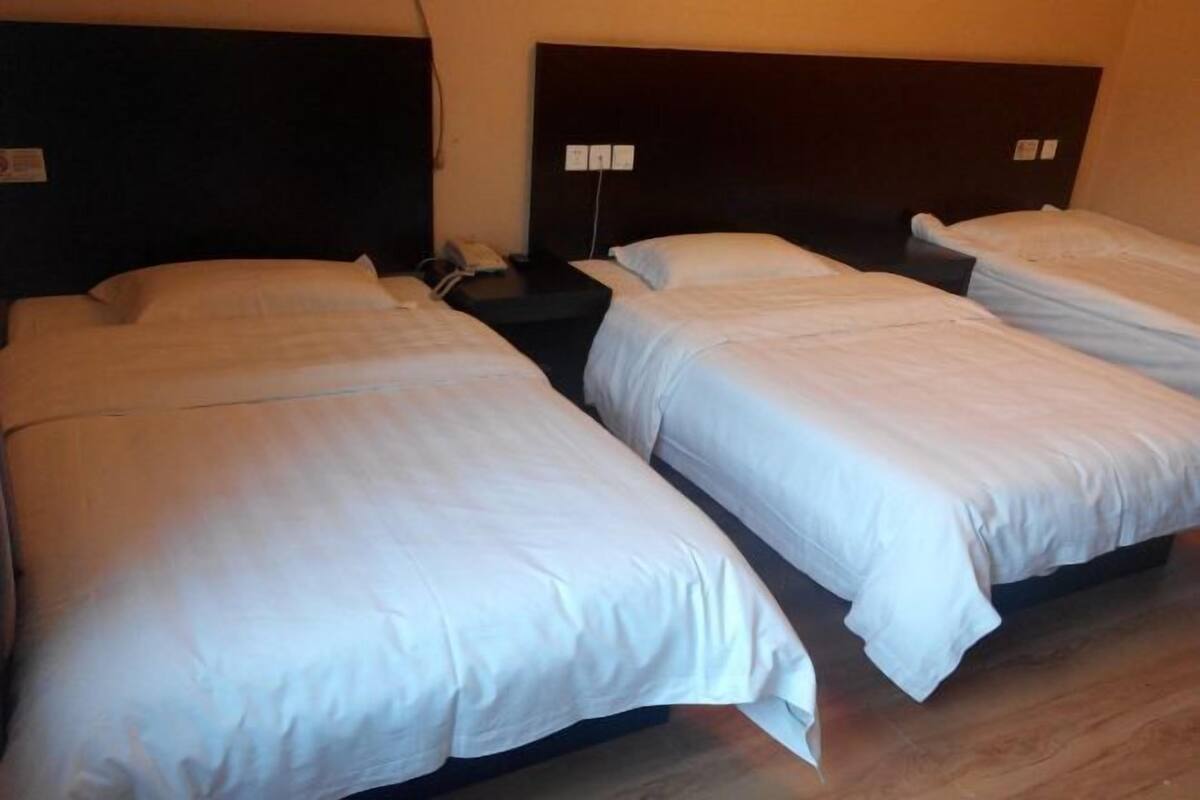Habitación de hotel con tres camas individuales, un cabecero oscuro, una mesita de noche con teléfono y un enchufe de pared.