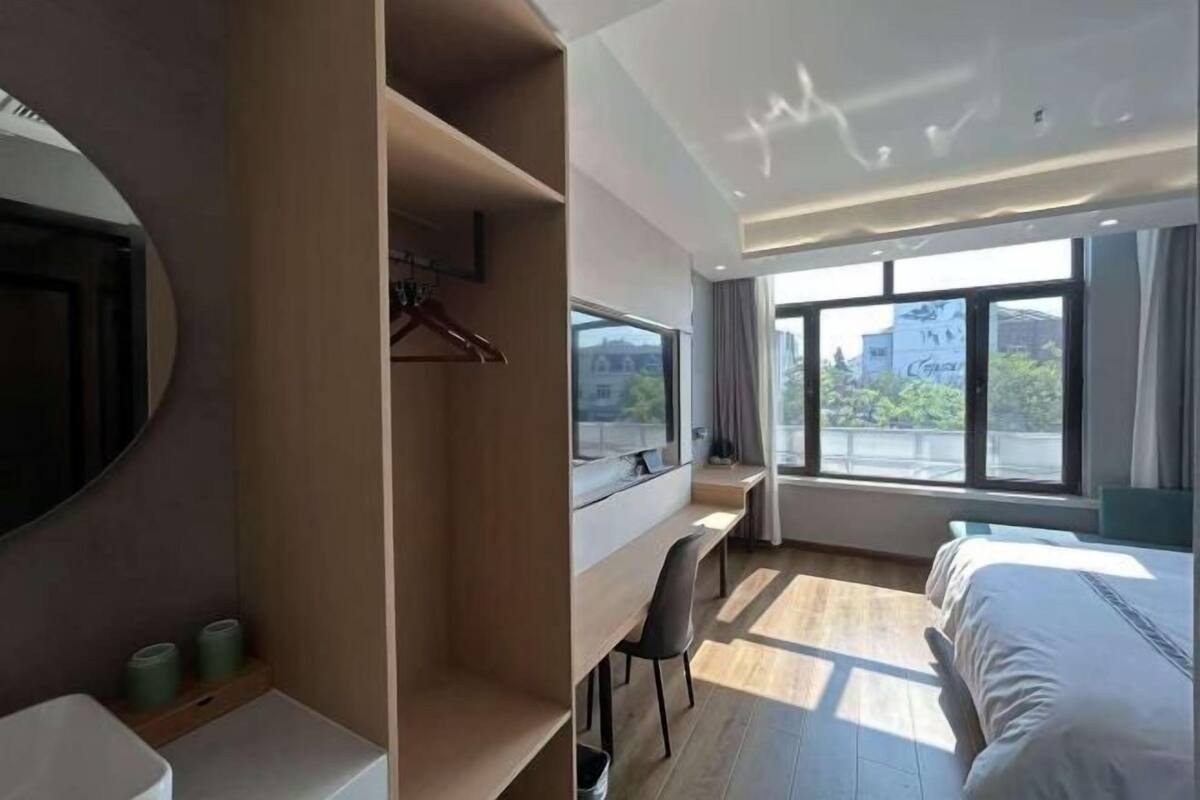 Una habitación de hotel con una cama, un escritorio, una silla, un ventanal grande y un espejo.