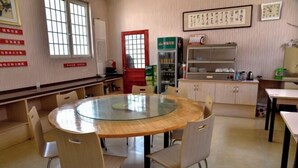 A round glass table with chairs in a room with light-colored walls, a red door, and shelves with items.
