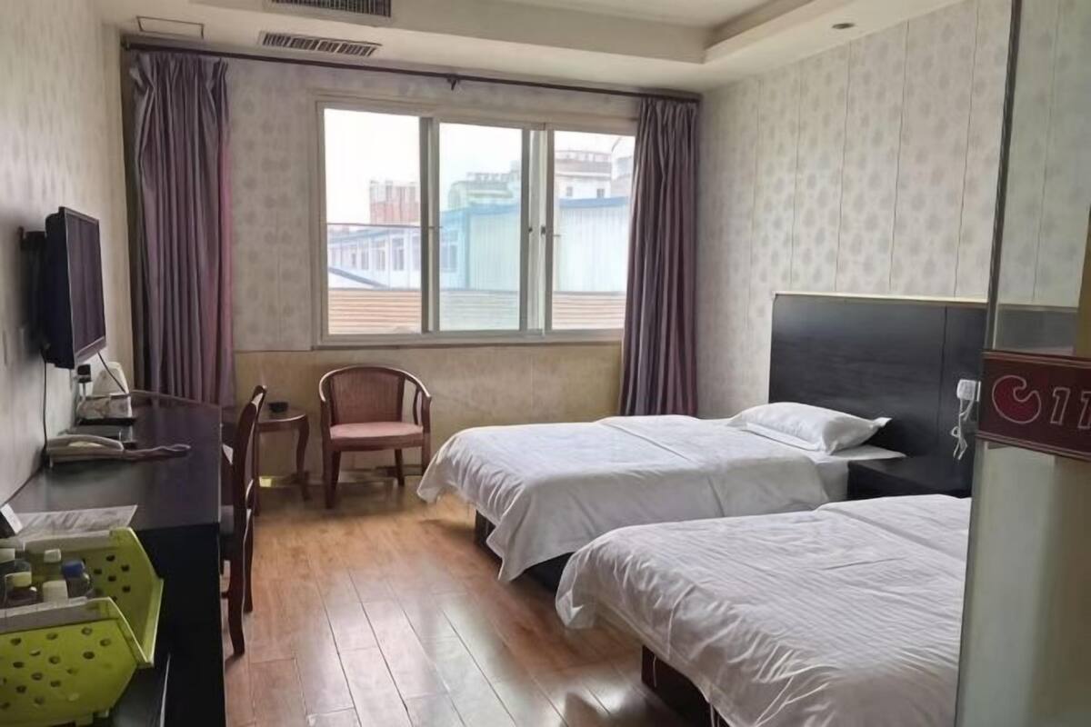 Habitación de hotel con dos camas, un escritorio con silla, televisor y ventana con cortinas.