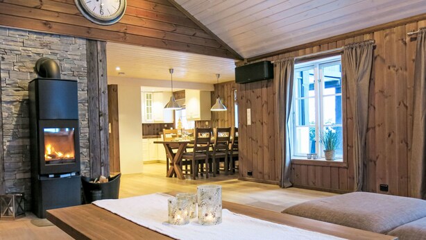 A cozy living room with a fireplace, wooden walls, a dining area, and a large window.