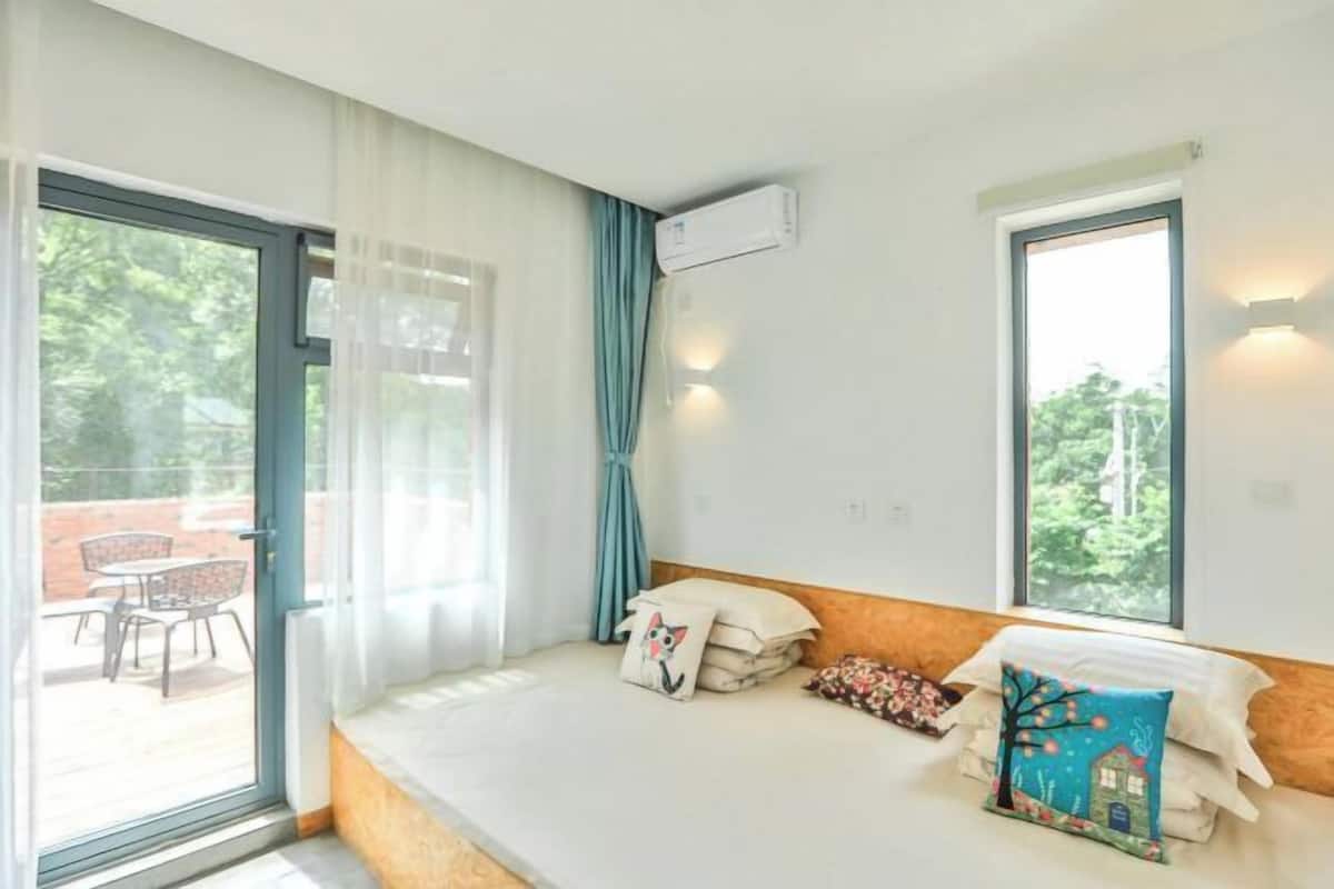 A room with a bed, a window, an air conditioning unit, and a view of the outdoors.