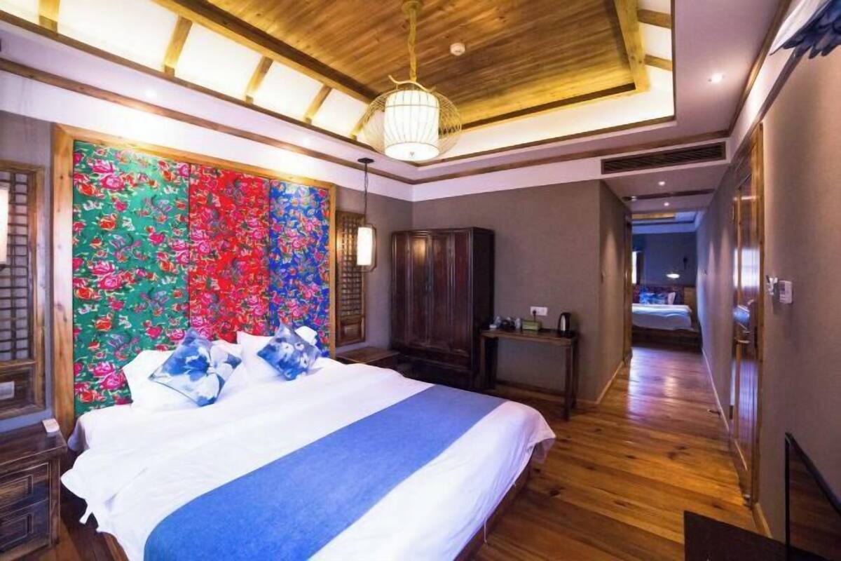 A bedroom with a bed, wooden floor, a wardrobe, and a hallway leading to another room.