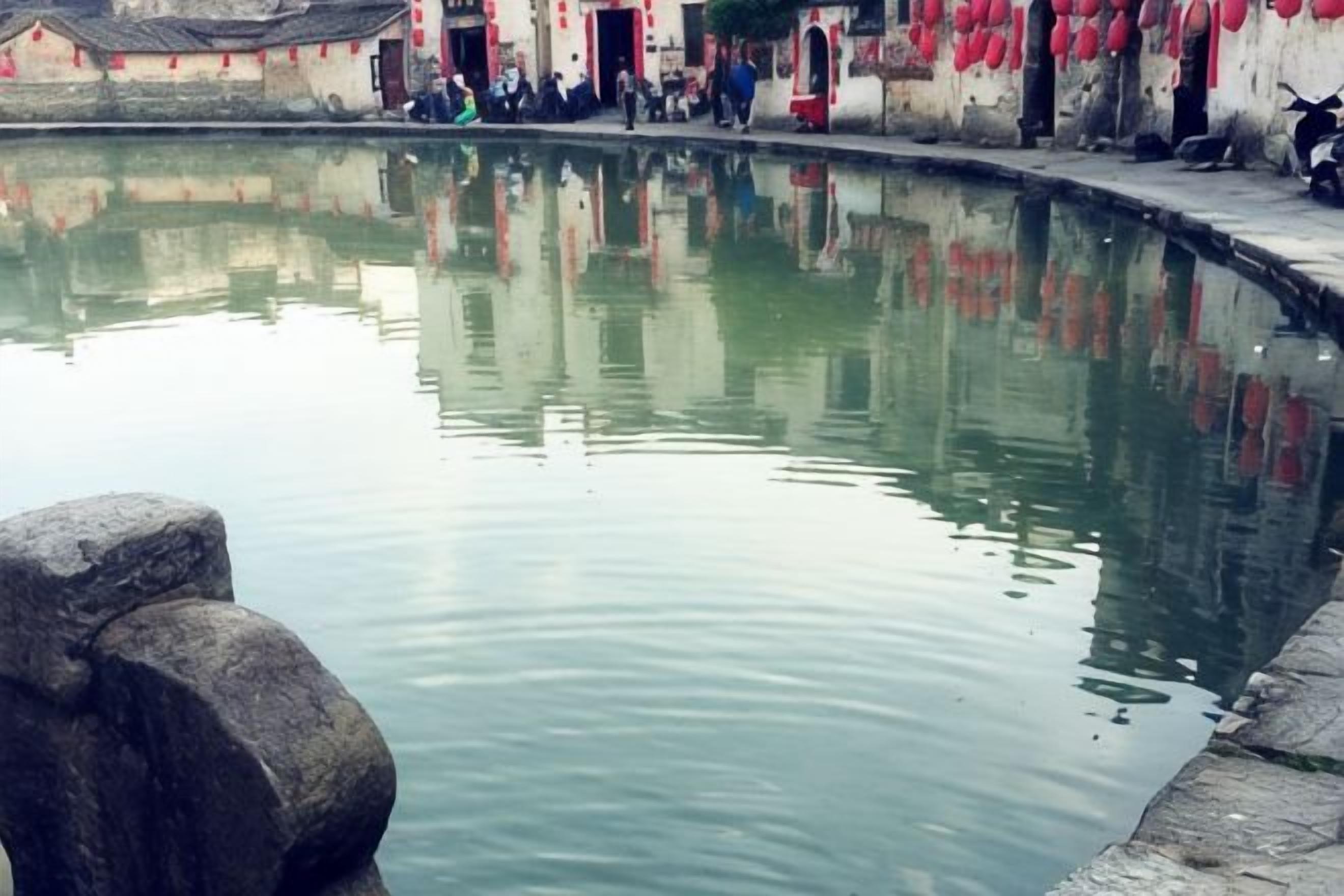 Una masa de agua tranquila con una estructura de piedra en primer plano, rodeada de edificios con detalles rojos.
