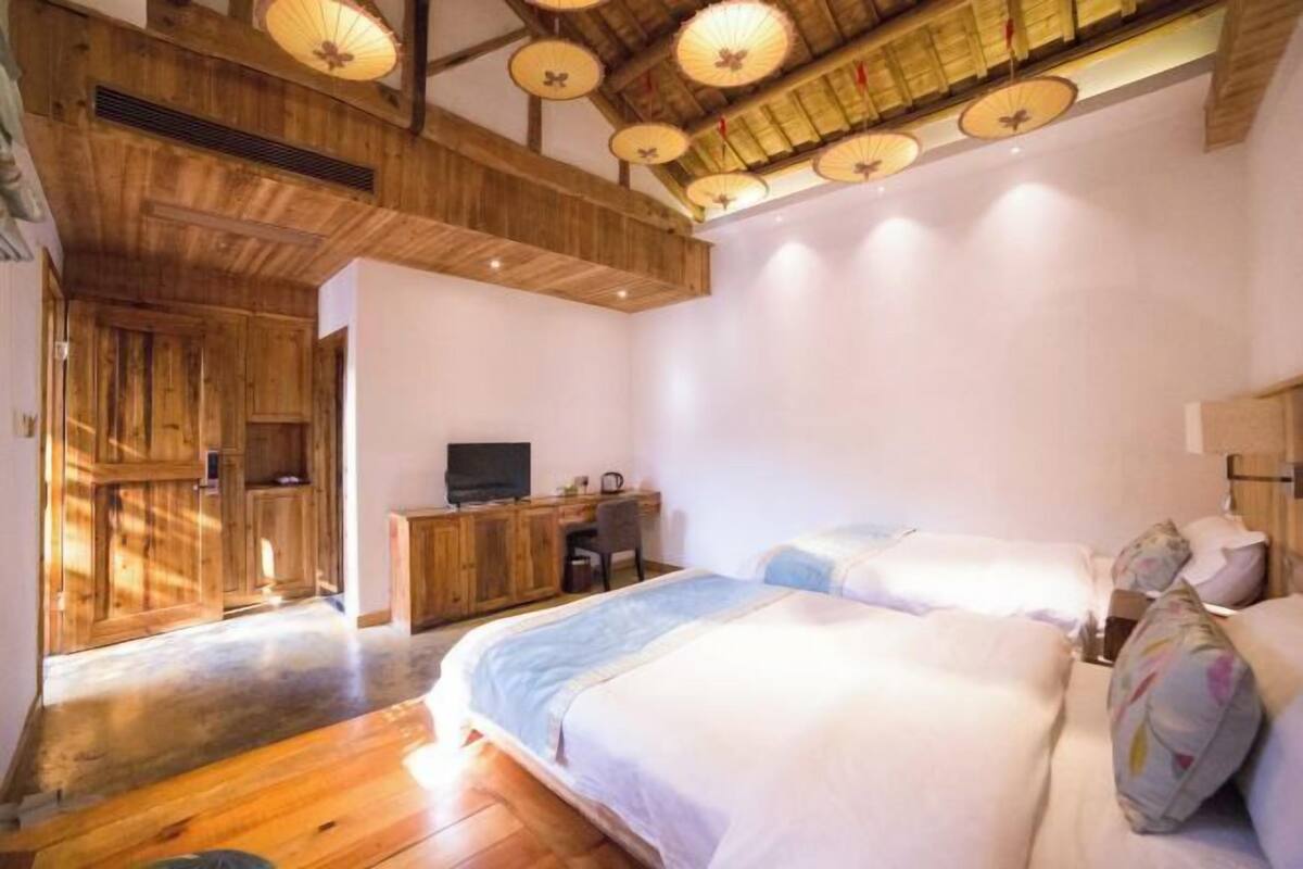 A bedroom with a wooden ceiling, a desk, a bed, and a television.