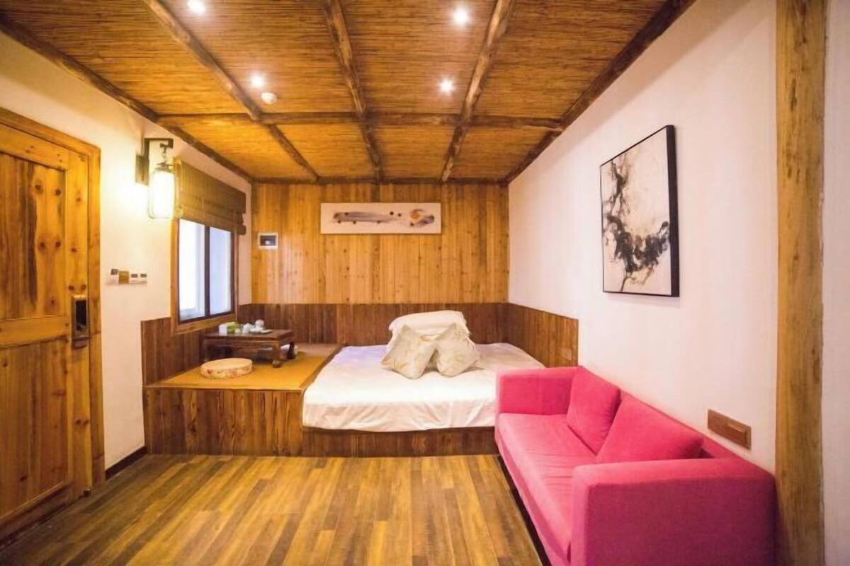 A room with a wooden ceiling, a bed with a white mattress, a pink sofa, and a wooden floor.