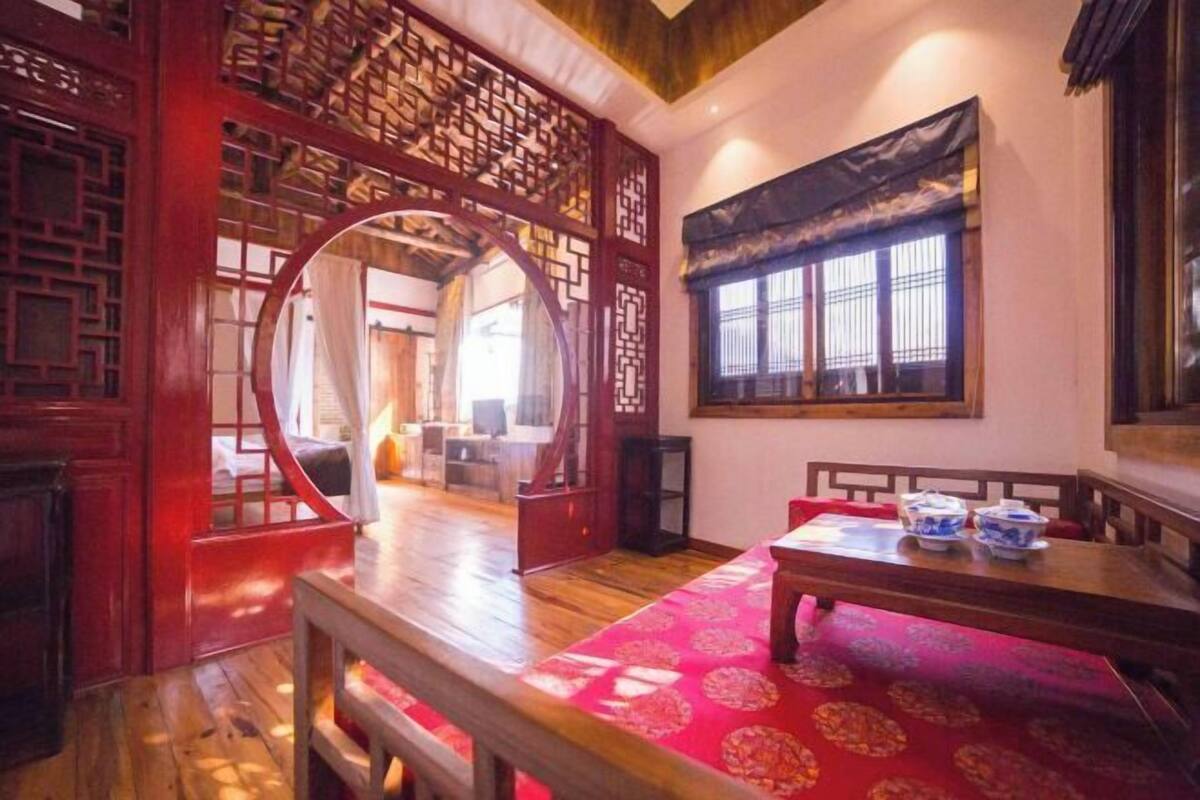 A traditional room with a wooden floor, a red patterned carpet, a dining table with bowls, and a window with a view.