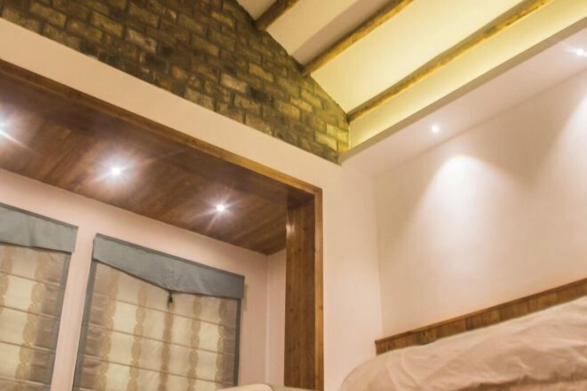 Una camera da letto con soffitto in legno, parete in mattoni e un letto con testiera bianca.