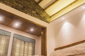 Una camera da letto con soffitto in legno, parete in mattoni e un letto con testiera bianca.