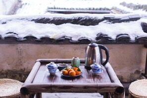 Un tavolo di legno con un teiera, tazzine e un piatto d'arance su un balcone con tegole coperte di neve.