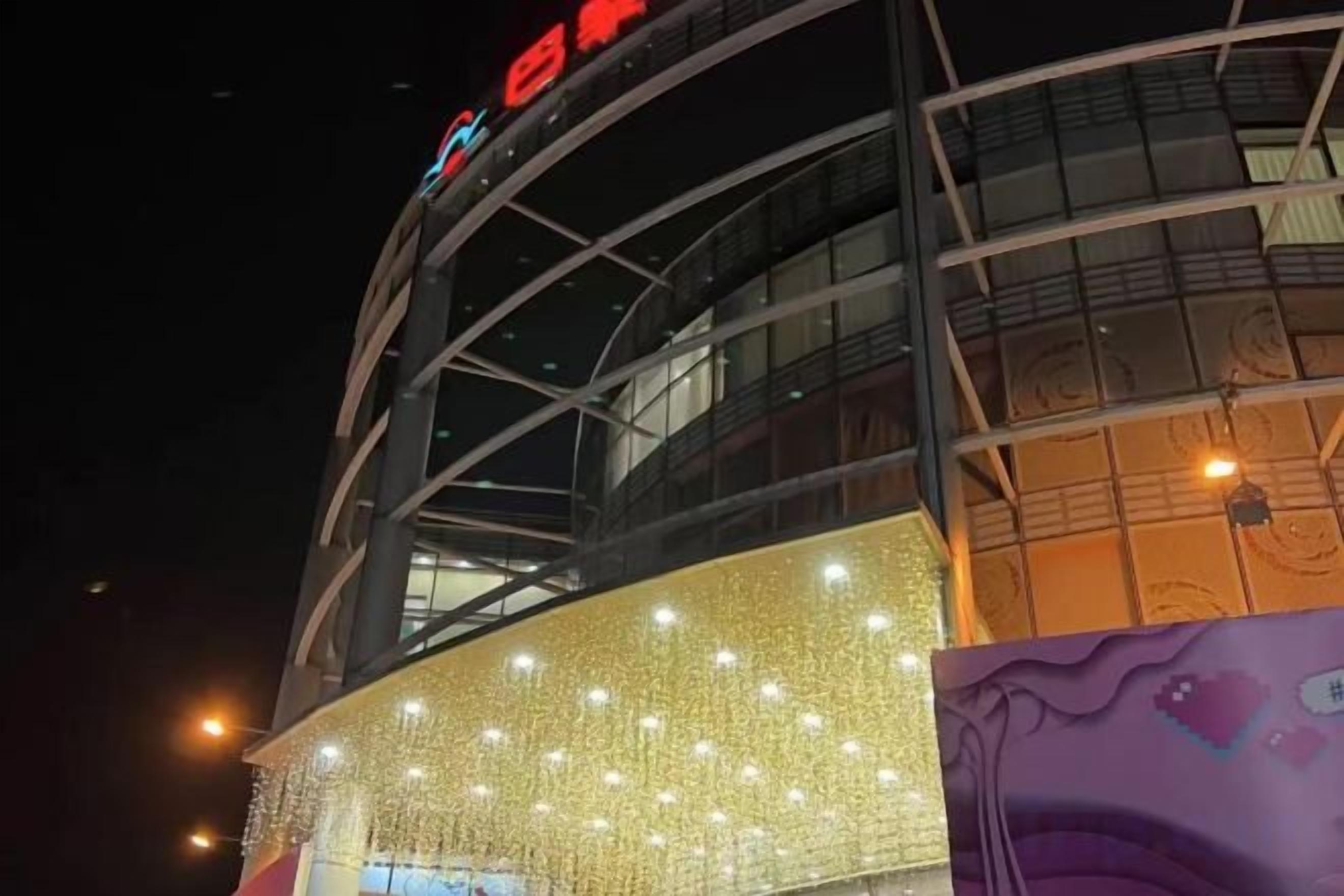 A building with a curved facade, illuminated by string lights and a large illuminated sign.