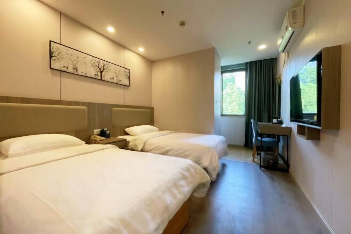 A hotel room with two beds, a desk, a chair, a painting on the wall, and a window with curtains.