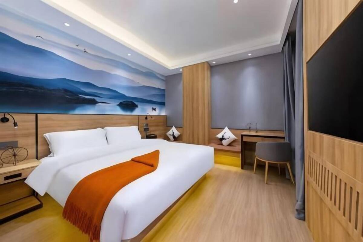 A modern hotel room with a large bed, a desk, and a mural on the wall.