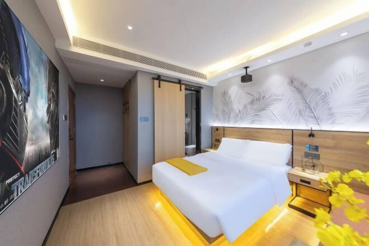 A modern hotel room with a bed, bedside table, and a wall with a feather pattern.