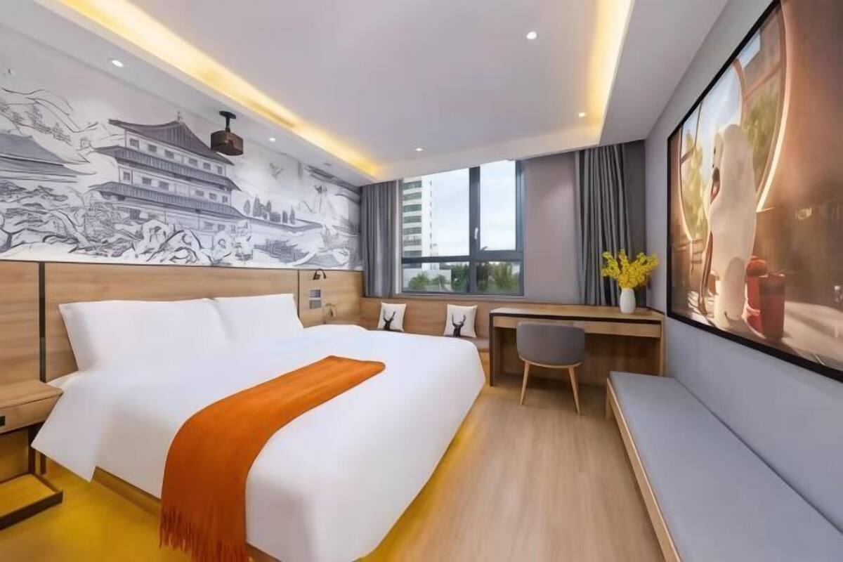 A hotel room with a bed, desk, and large windows.