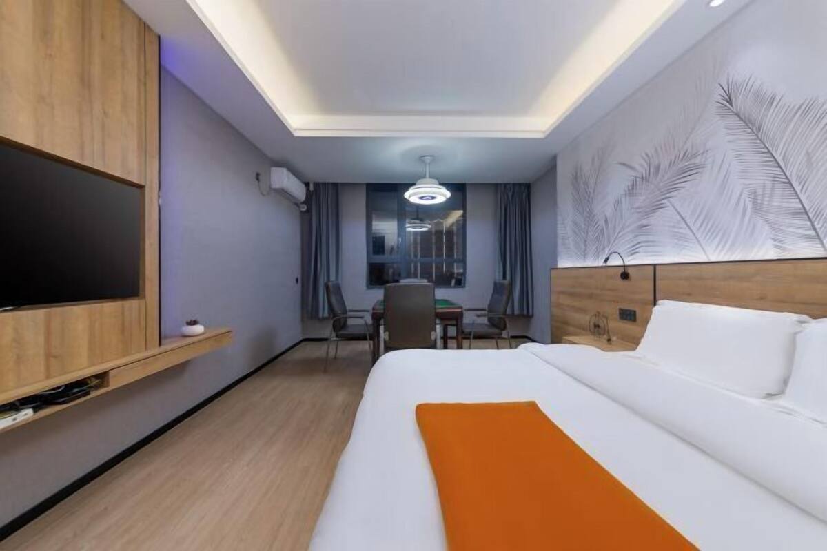 A hotel room with a bed, a TV, a desk with chairs, and a view of the city.