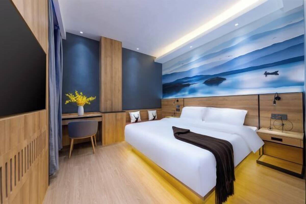 A modern hotel room with a large bed, a desk, and a wall mural.
