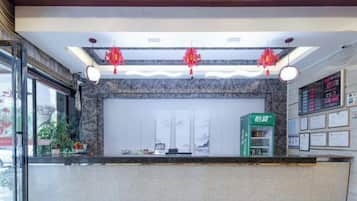 Zona de recepción de hotel con mostrador de mármol, un quiosco de información verde y una pantalla informativa digital.