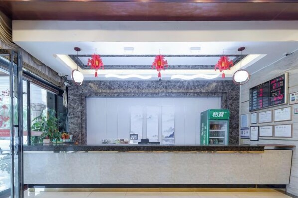 A hotel reception area with a marble counter, a green information kiosk, and a digital display board.