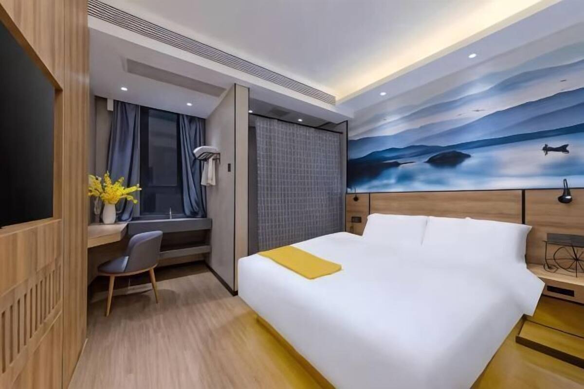 A hotel room with a bed, desk, chair, and a large painting on the wall.