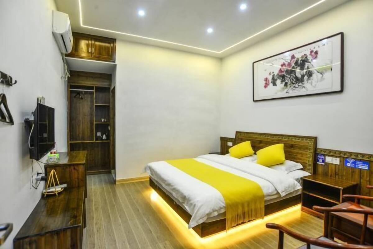 Quarto de hotel com cama, mesa de cabeceira, cadeira, televisão, guarda-roupa e obra de arte na parede.