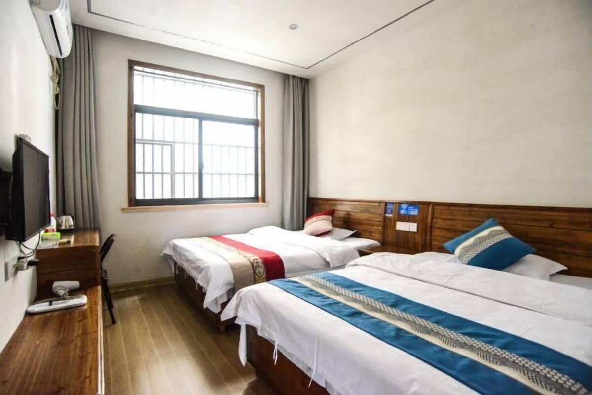 Quarto de hotel com duas camas, uma escrivaninha com cadeira, televisão e uma janela grande.