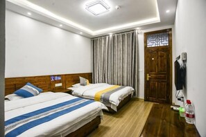 Une chambre d’hôtel avec deux lits, des têtes de lit en bois, un plancher en bois, une fenêtre avec des rideaux et une porte ornée d’un panneau de verre décoratif.