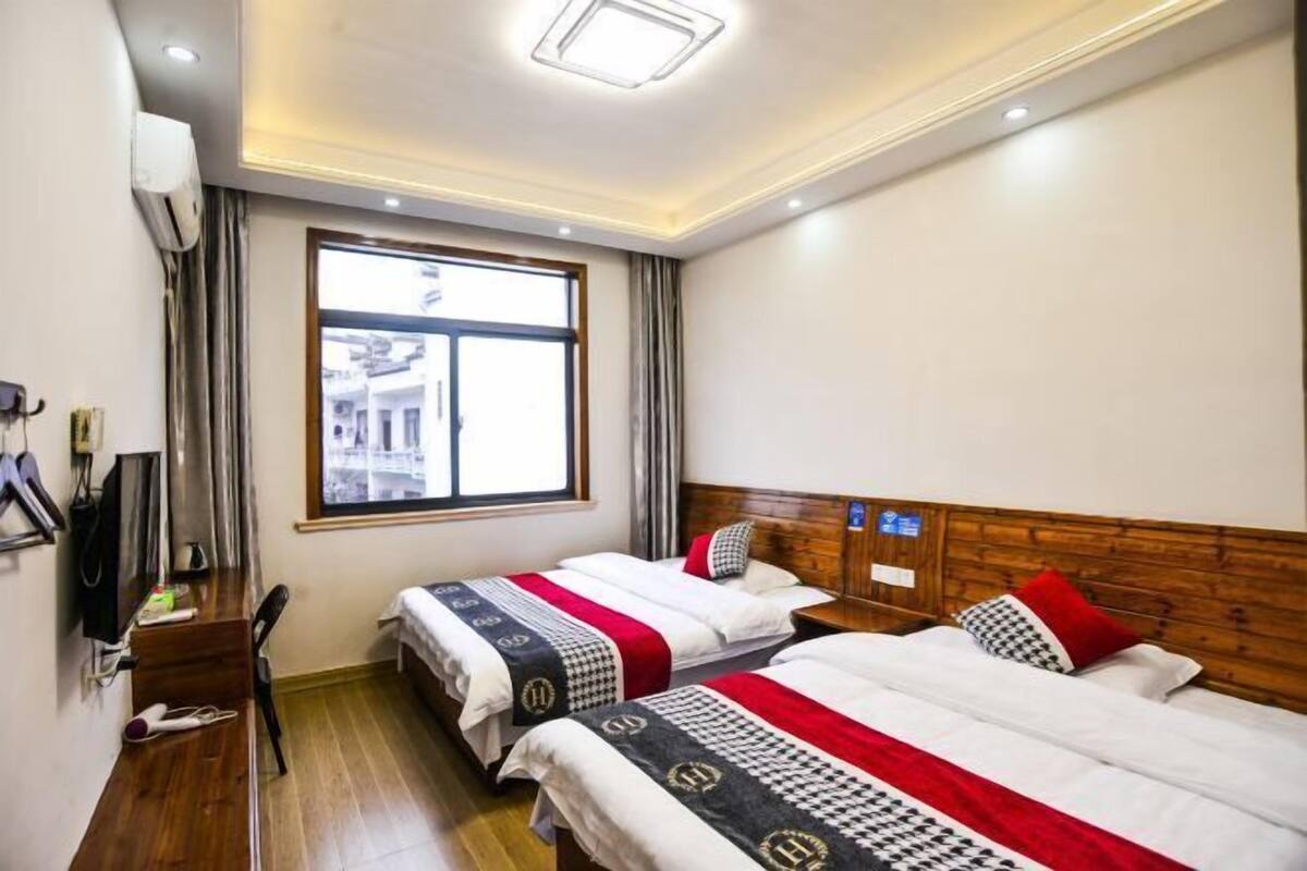 Quarto de hotel com duas camas, uma escrivaninha, uma cadeira, janela com cortinas e iluminação no teto.