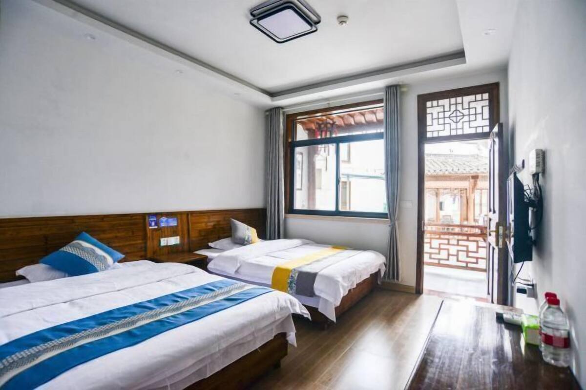 Quarto de hotel com duas camas, cabeceira de madeira, janela com cortinas e vista para um edifício tradicional.
