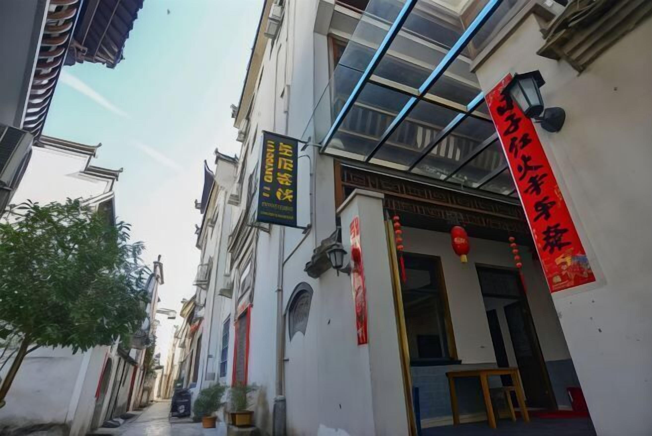 A narrow street with traditional architecture, a visible storefront with a red sign, and a clear sky.