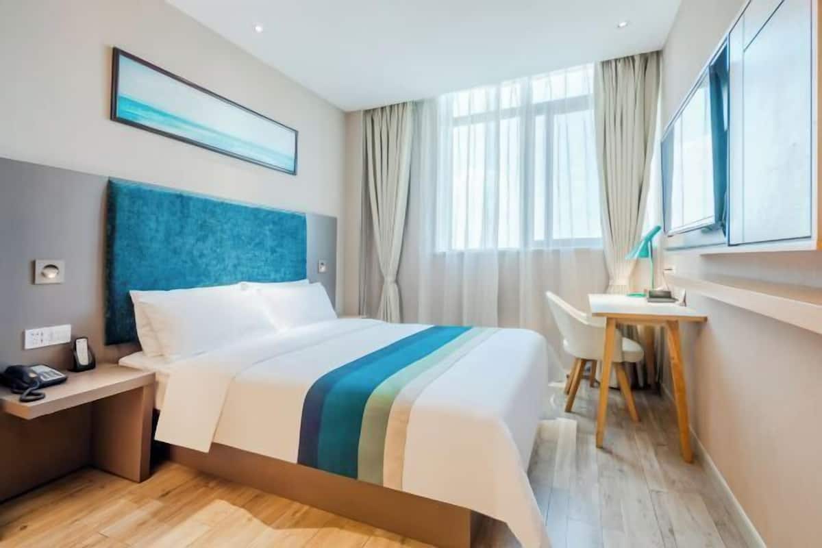 A modern hotel room with a large bed, a desk, and a view of the city.