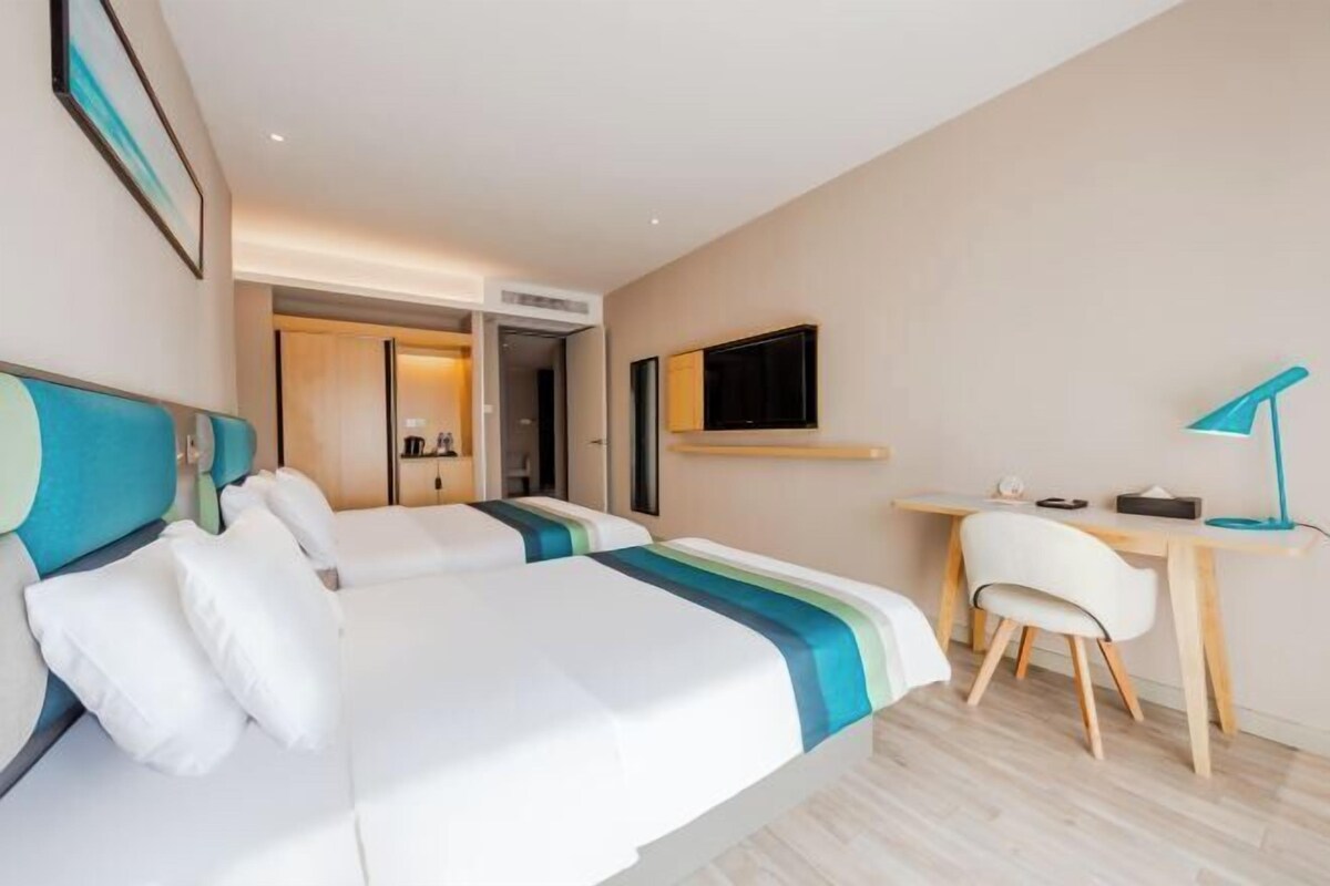 A hotel room with two beds, a desk, a chair, a TV, and a door leading to a bathroom.
