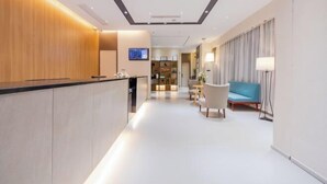 Eine moderne Hotelhalle mit einer Rezeption, einer Lounge und einer Treppe zu den oberen Stockwerken.