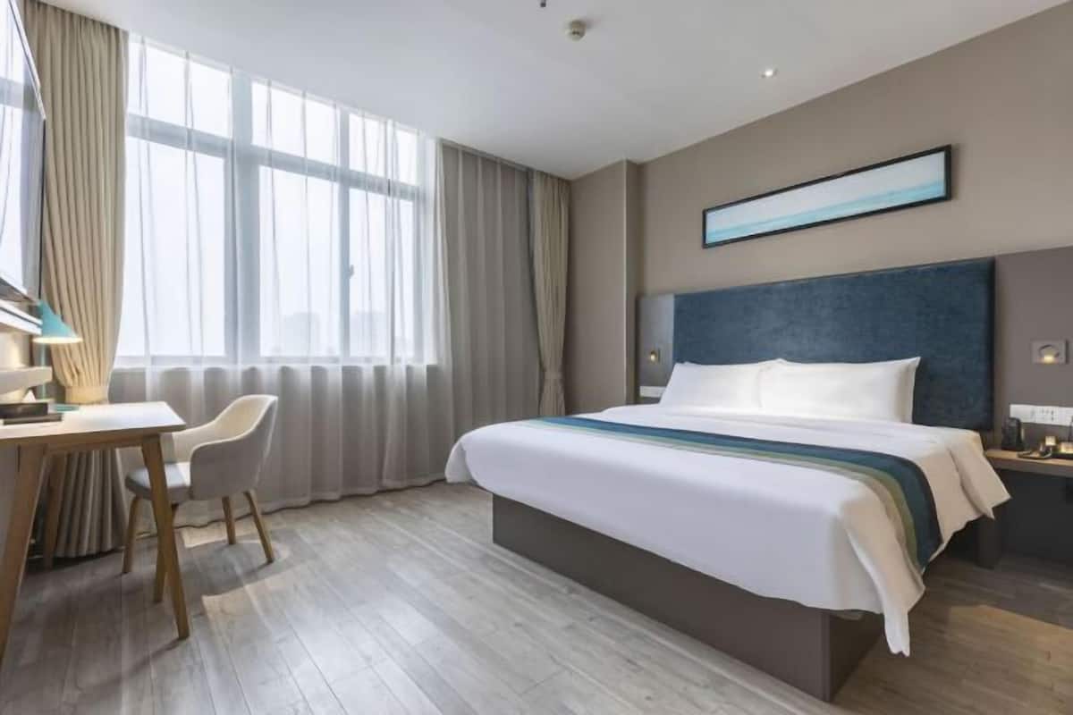 A modern hotel room with a large bed, a desk, and a chair.