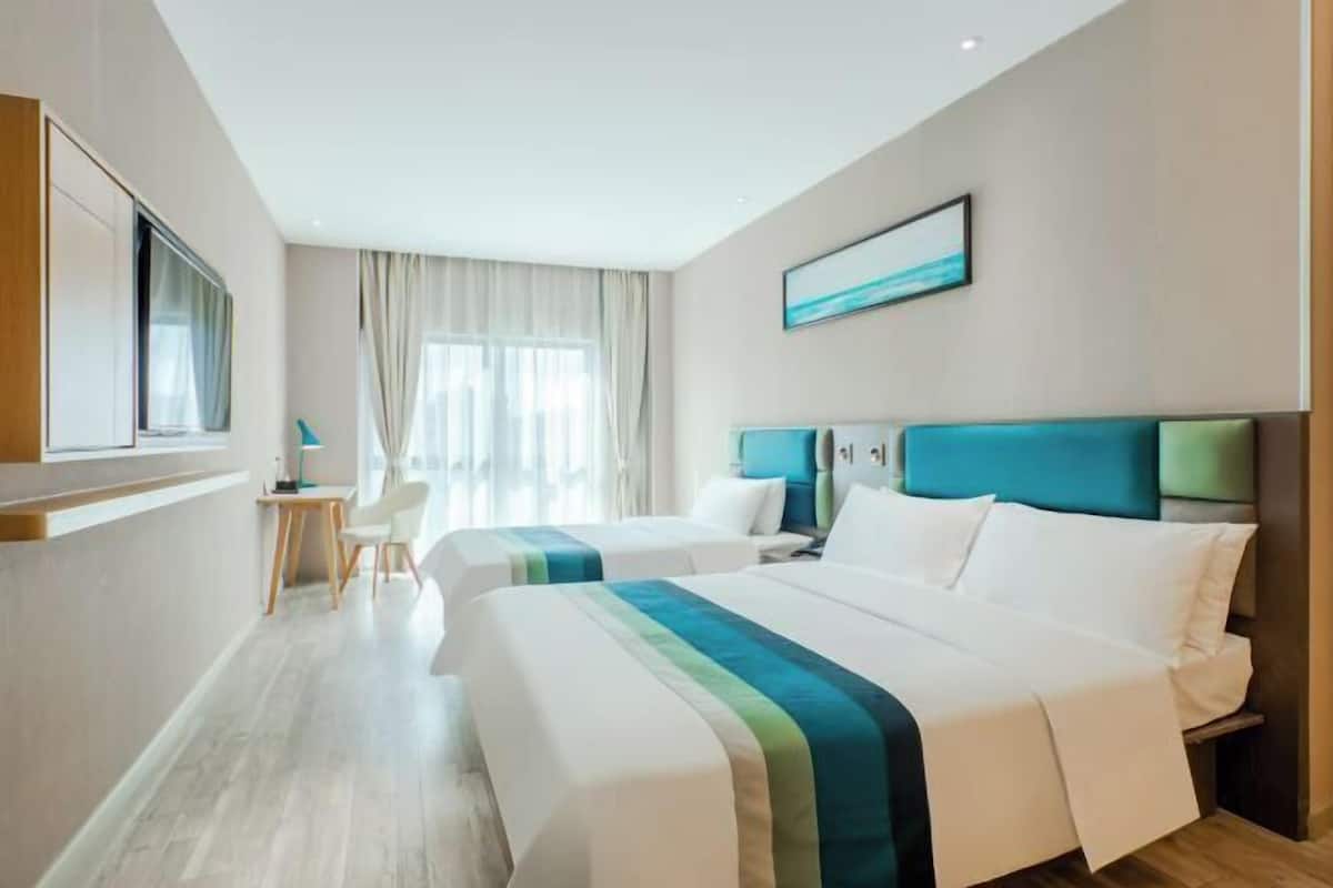 A hotel room with two beds, a desk, and a window with curtains.