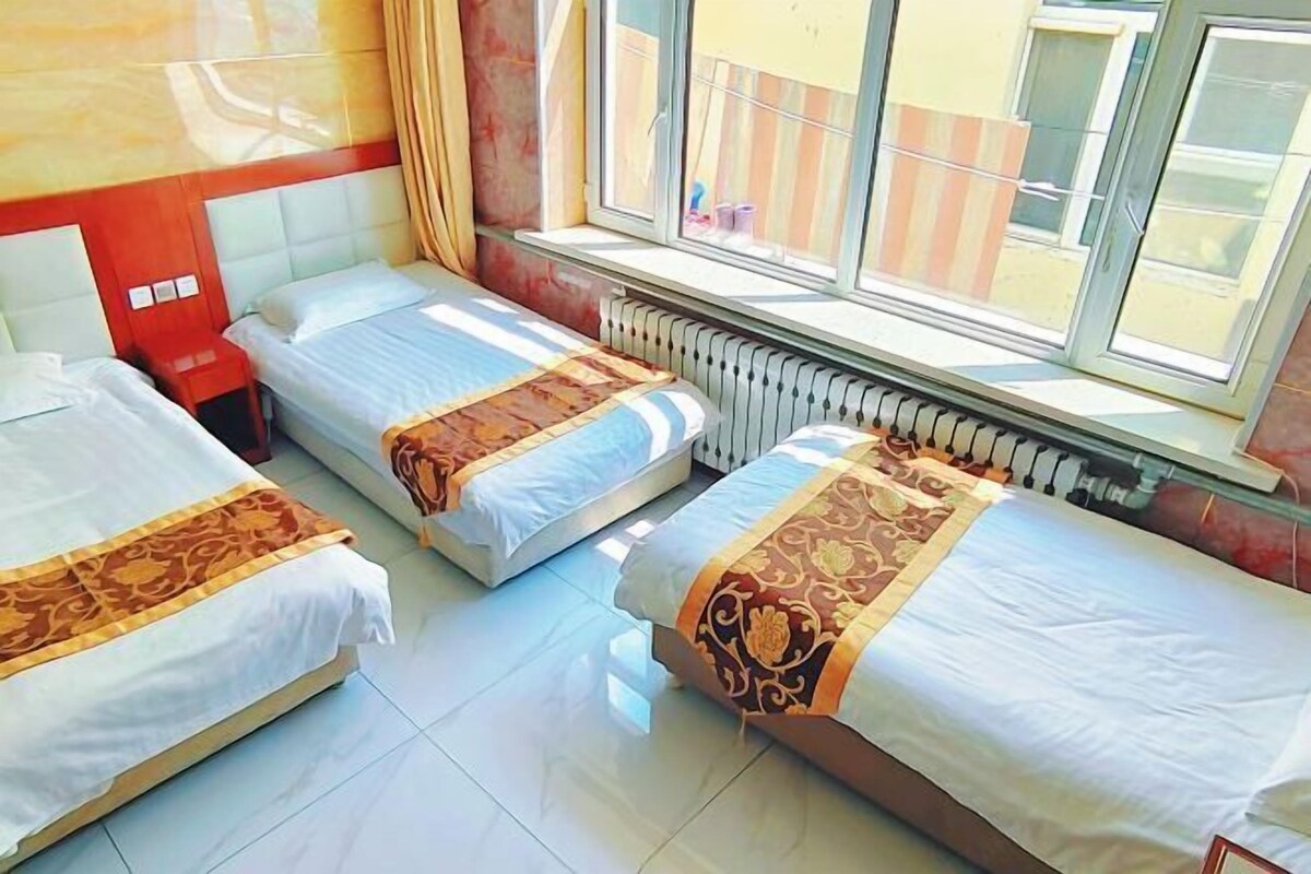Una habitación de hotel con tres camas, una ventana con cortinas y un radiador.