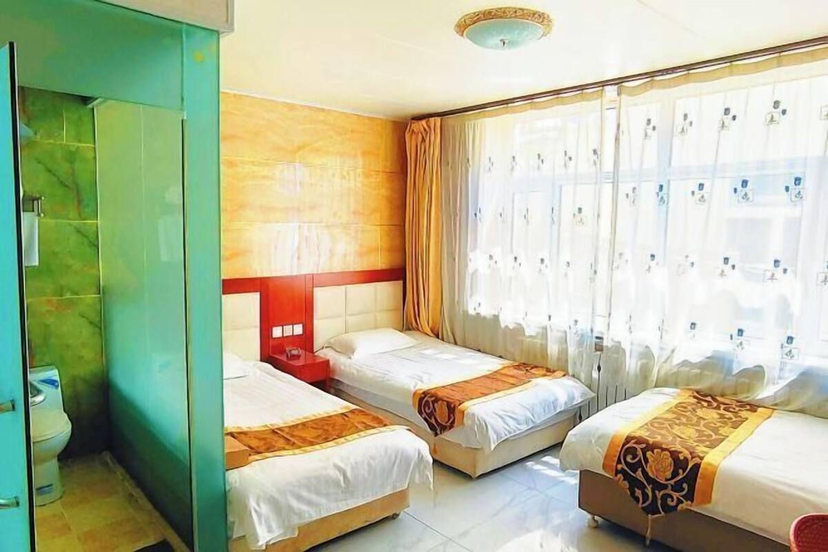 Ein Hotelzimmer mit zwei Einzelbetten, einem roten Kopfteil, einem großen Fenster mit Vorhängen und einer grünen Wand.