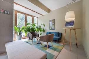 Una habitación de hotel moderna con una cama, un sofá, una silla, un escritorio con lámpara y ventanas amplias.