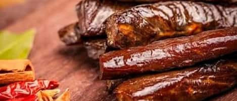 Una pila de salchichas secas y oscuras sobre una superficie de madera, con anís estrellado y palitos de canela cerca.