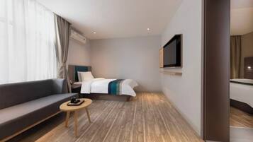 Una habitación de hotel moderna con sofá, una pequeña mesa redonda, una cama con manta a rayas blancas y azules, un televisor montado y suelo de madera.