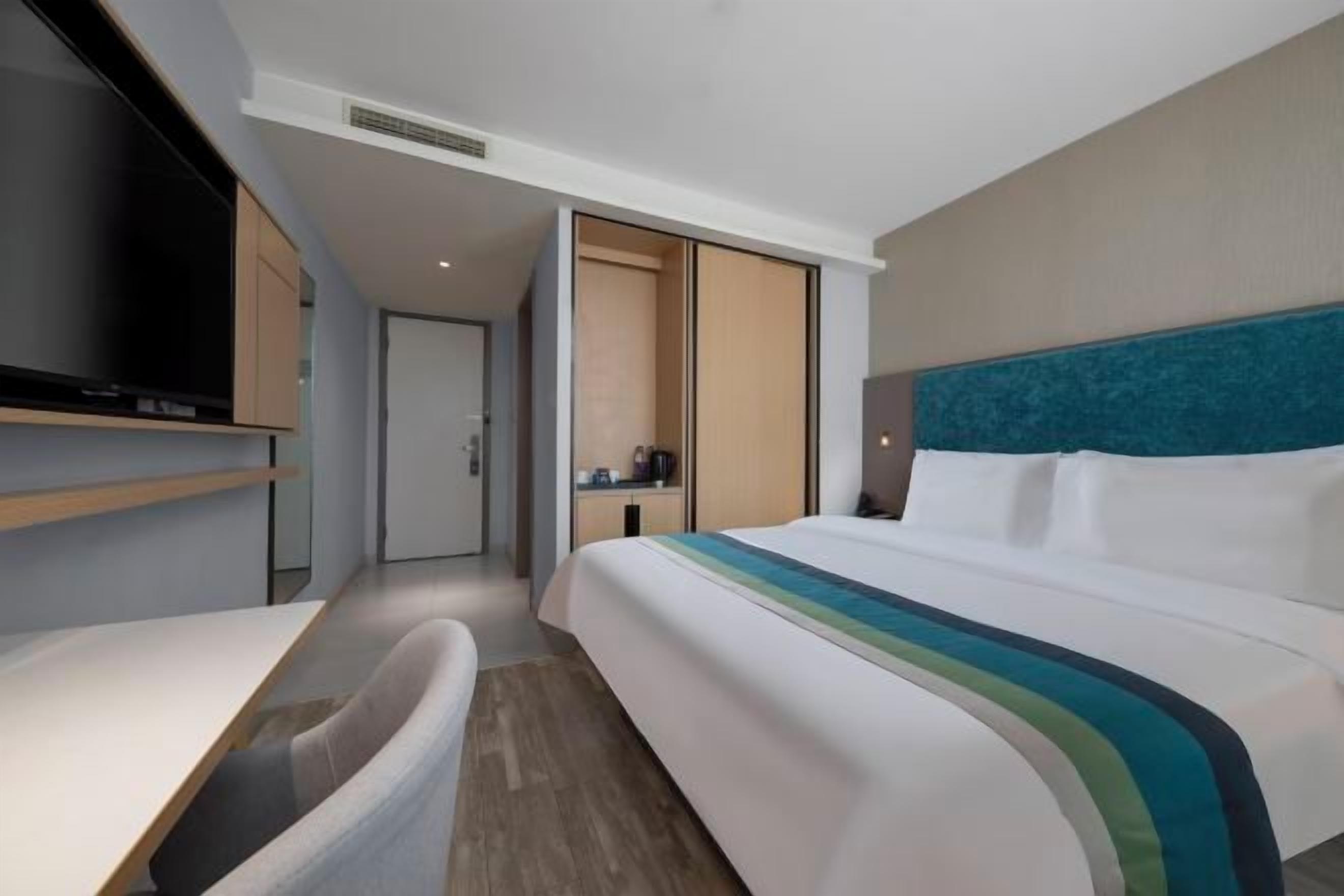 A modern hotel room with a bed, a desk, and a TV.