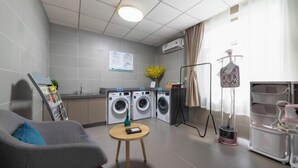 Een moderne, goed verlichte kamer met een grijze bank, een klein rond tafeltje, een wasmachine, een droogrek en een mannequin.