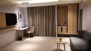 Una habitación de hotel moderna con una televisión de pantalla plana, un escritorio, una silla, un sofá, una mesita redonda y un armario.