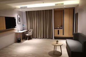 Una habitación de hotel moderna con una televisión de pantalla plana, un escritorio, una silla, un sofá, una mesita redonda y un armario.